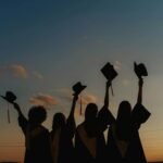 A group of graduates celebrate by raising their caps against a vibrant sunset sky, symbolizing achievement.