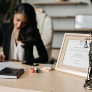 Focused woman writing at desk with Lady Justice figurine and certificate in office.