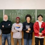 A diverse group of students and a teacher smiling in front of a chalkboard filled with formulas.