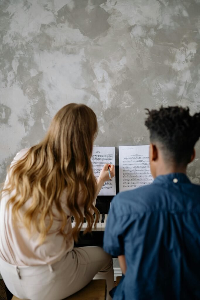 Back view of a woman teaching a child piano, focusing on musical notes.