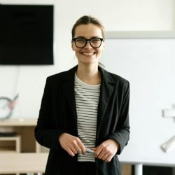 pexels-photo-6981008-6981008 Caucasian woman in black blazer with eyeglasses, smiling in classroom.